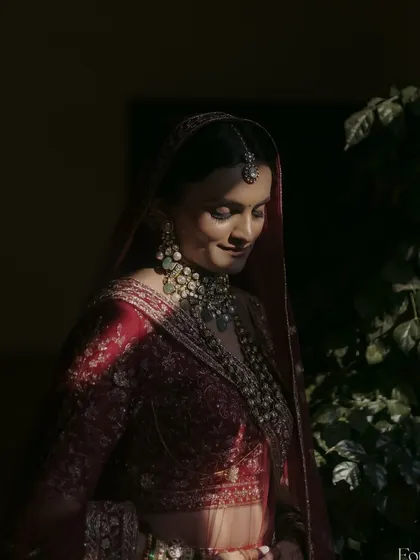 A dramatic and artistic shot of the bride. The play of light and shadow highlights the contours of her face and the richness of her red Pheras outfit.