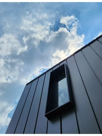 An upward-looking shot of a modern office building's facade. The clean grey paneling and minimalist window design reflect a professional and contemporary business image.
