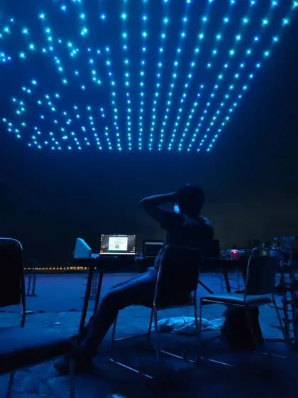 A pilot sits at their station, surrounded by the blue glow of hundreds of drones ready for flight. This image captures the calm focus required to command a fleet and paint a masterpiece in the sky.