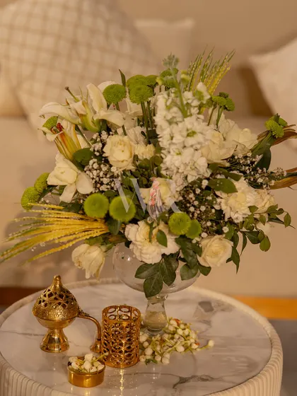 A simple, elegant detail. A bouquet of white lilies and carnations in a glass vase, placed next to a traditional brass incense burner, filling the air with a beautiful, subtle fragrance.