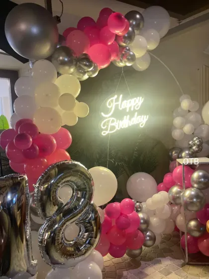 A chic 18th birthday celebration with a pink, white, and silver color scheme. The balloon-covered ring and large foil numbers create a perfect photo opportunity.