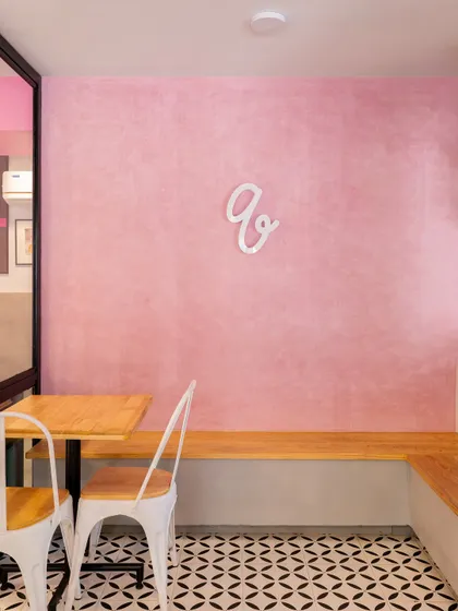 A minimalist seating nook inside Qoqobae. The textured pink wall, simple wooden bench, and the brand's logo create a clean, photo-worthy corner that is both functional and aesthetically pleasing.