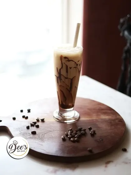 A refreshing glass of our signature cold coffee, perfectly framed by the window light in our cozy cafe.