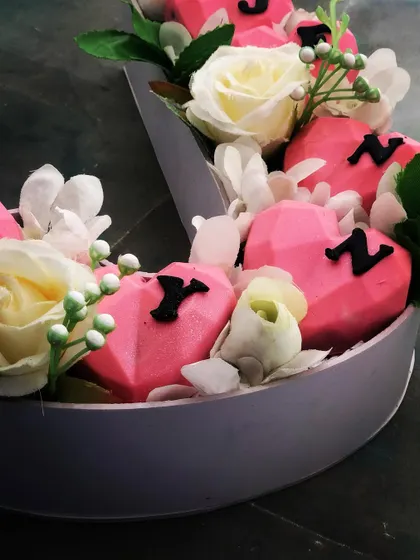 A closer view of our cakesicle bouquet shows monogram letters on pink hearts, with floral details framing the personalised gift.