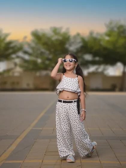 An outdoor shot capturing a carefree, sunny day vibe. Her polka-dot outfit and white sunglasses give off a cool, retro feel. This photo shows how we can take stylish portraits outside the studio, using natural light and settings.