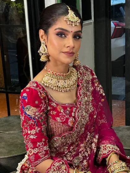 A full view of this stunning bridal look. The makeup is balanced to complement the heavy embroidery of the lehenga and the intricate jewelry, with a sleek hairstyle to keep the focus on her face.