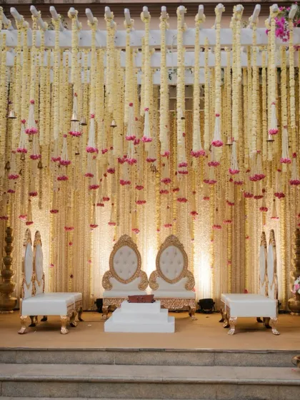 A closer look at the mandap seating, featuring ornate white and gold chairs set against a backdrop of thousands of delicate floral strings. The design exudes a sense of quiet luxury and grace.