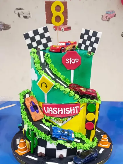 An exciting two-tiered Cars track cake, with a winding road and toy cars for a dynamic and playful birthday.