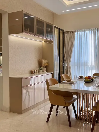 This dining space is seamlessly connected to the kitchen, featuring a custom crockery unit with under-cabinet lighting. The stone-top dining table with its gold metal base and tan leather chairs creates a warm, modern, and effortlessly luxe atmosphere.