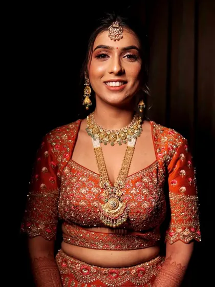 A portrait of the bride against a dark background, making her orange lehenga and glowing makeup pop.