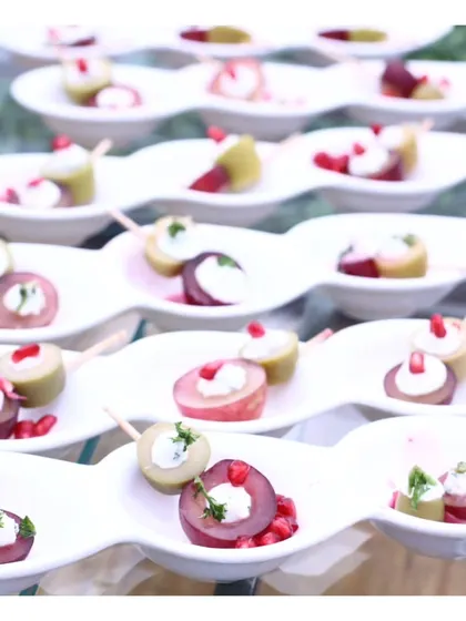An elegant platter of fruit and cheese skewers, featuring plums, olives, and cream cheese, garnished with pomegranate seeds.