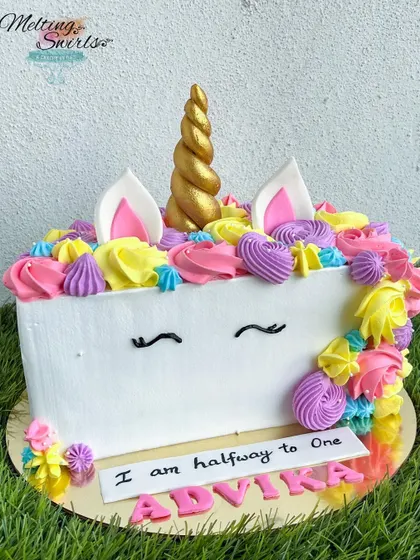A magical unicorn-themed half-birthday cake. This design features a colorful mane of whipped cream swirls and a golden fondant horn, perfect for a six-month celebration.