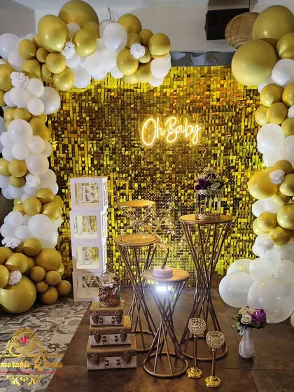 A glamorous 'Oh Baby' setup for a baby shower, featuring a gold shimmer wall and an organic arrangement of gold and white balloons.