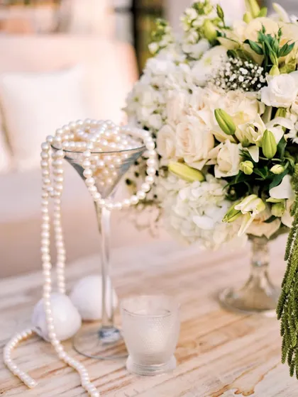 A beautiful detail shot of the pearls spilling from a martini glass, a nod to classic glamour. This sits beside a fresh arrangement of white roses and lilies.