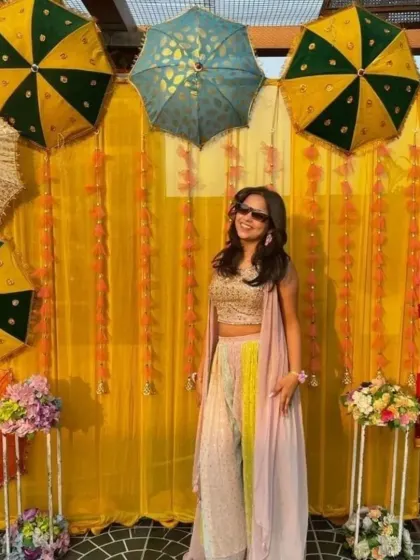 A fun photo booth for a Haldi ceremony. The backdrop is a simple yellow curtain decorated with marigold strings and colorful umbrellas.