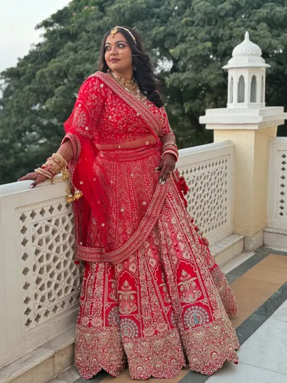 This full-length portrait showcases the grandeur of a traditional red bridal lehenga. The makeup is balanced to complement the heavy embroidery and jewellery, creating a cohesive and regal look.