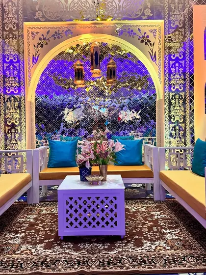 A Turkish-inspired seating lounge with white wooden furniture, vibrant blue cushions, and a backdrop of intricate mirror work and latticework arches.