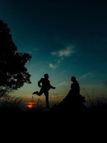 A playful sunset silhouette of a couple on a hilltop. The groom's joyful leap towards the bride creates a fun and dynamic pre-wedding picture.
