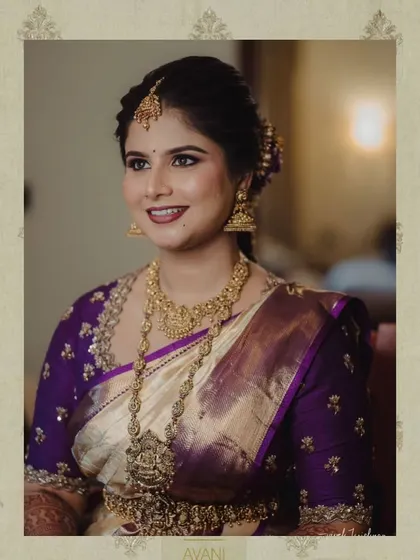 A bride in a cream and purple Kanchipuram saree. Her custom purple blouse is adorned with delicate gold embroidery, perfectly matching her temple jewelry.