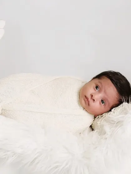 A serene portrait of an awake newborn resting in a white moon prop. The simple, all-white setup with soft fur creates an angelic and dreamy atmosphere.