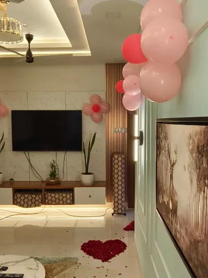 A wider view of a living room decorated for a baby girl's homecoming. The space is thoughtfully arranged with balloons and flower petal hearts to create a warm and loving environment.