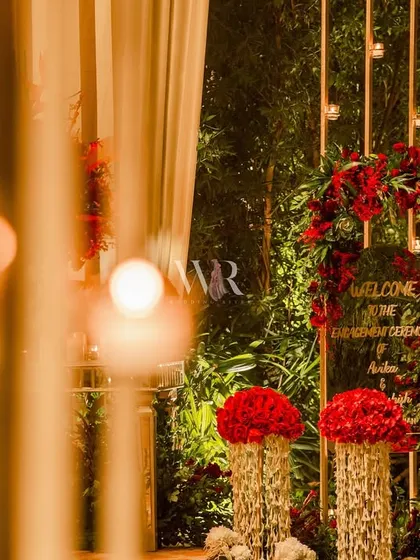 A beautiful welcome installation designed to be picture-perfect from every angle. A custom acrylic sign is framed by a wreath of rich red roses, with elegant floral pillars standing alongside, creating a luxurious first impression for guests.