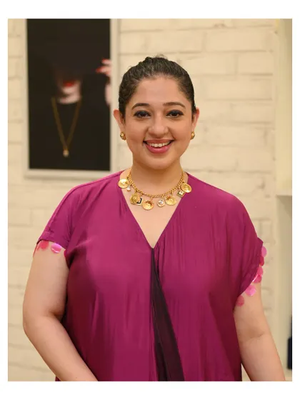 A guest radiates joy as she wears a gold coin necklace from our JJ Valaya collection. Our studio provides the perfect backdrop for finding pieces that make you smile.