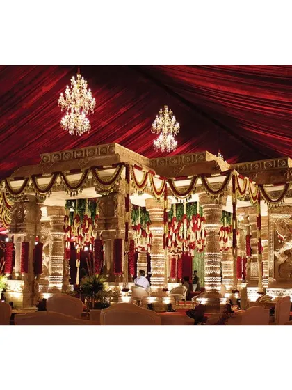 Another perspective of the grand mandap, highlighting the interplay of light on the carved pillars and the rich textures of the floral arrangements. The chandeliers add a touch of modern luxury to the traditional structure.