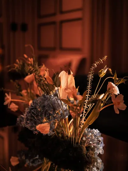 A detail shot of a floral arrangement in the warm, ambient light of the evening. The composition of ferns, hydrangeas, and other delicate blooms adds a touch of organic beauty to the sophisticated party decor.