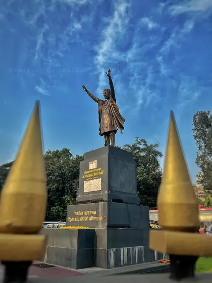 The statue of Balasaheb Thackeray viewed through the golden spires of a fence, adding a unique frame to the powerful monument.