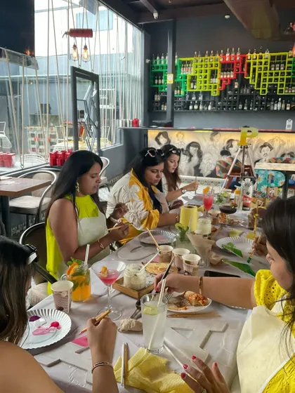 A view of the whole table at a kitty paint party. Everyone is engaged in their artwork, sipping drinks, and enjoying the social, creative atmosphere.