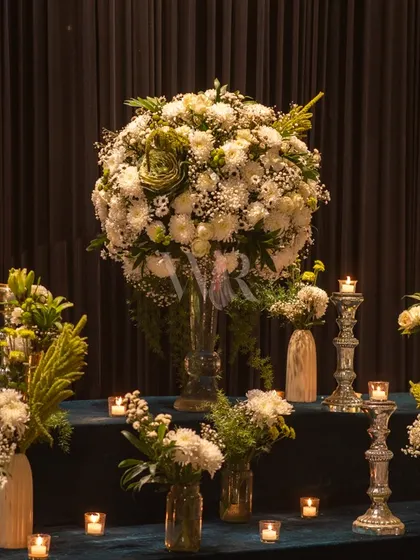 A classic floral arrangement of white chrysanthemums and baby's breath, surrounded by the warm flicker of tealight candles. This timeless combination adds elegance to any setting.
