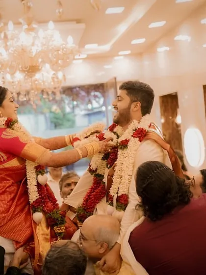 The bride and groom, lifted high, playfully exchange garlands in a moment of fun and friendly competition.
