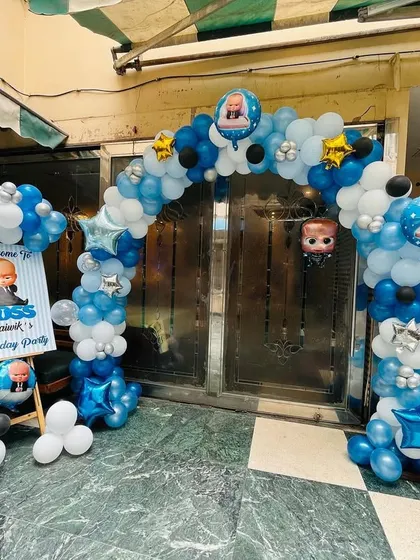 An outdoor entrance decoration for a "Boss Baby" themed birthday party, featuring a balloon arch and character cutouts.