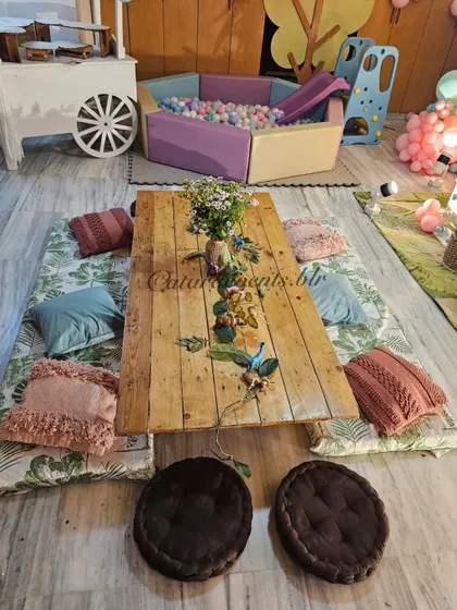 Low picnic-style seating with leaf-print mats and colorful cushions creates a cozy and kid-friendly dining area, with a ball pit visible in the background.