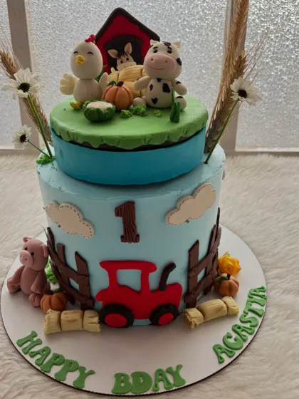 A two-tier farm animal cake for a first birthday. It features a red tractor, a fence, and adorable fondant animals, creating a charming barnyard scene.