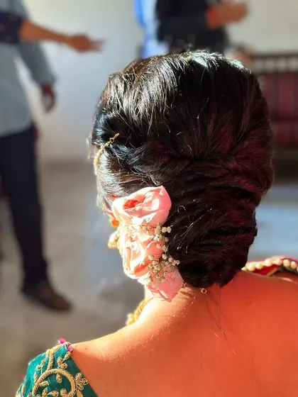 A classic low bun adorned with fresh pink roses and a delicate pearl nath-to-hair chain. This hairstyle is the epitome of grace and is perfect for a traditional wedding ceremony.