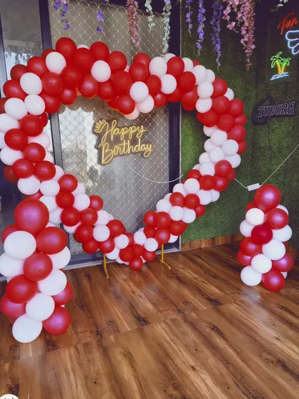 A classic and bold heart-shaped balloon arch made with red and white balloons. The wooden 'Happy Birthday' sign adds a rustic touch to this vibrant and cheerful party decoration, suitable for any indoor space.