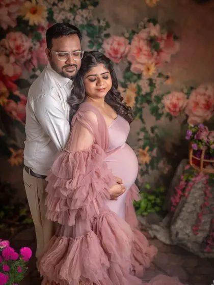 An expecting couple embraces lovingly in a studio decorated with flowers. The soft lighting and romantic setting make this a beautiful and intimate maternity portrait.