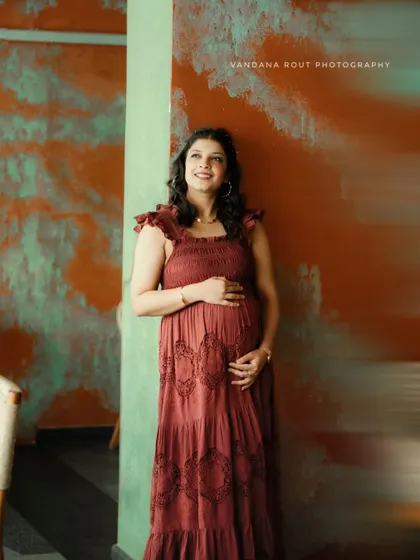 A full-length portrait of a mother-to-be in a beautiful boho dress, looking up with a hopeful and radiant expression in a rustic indoor setting.