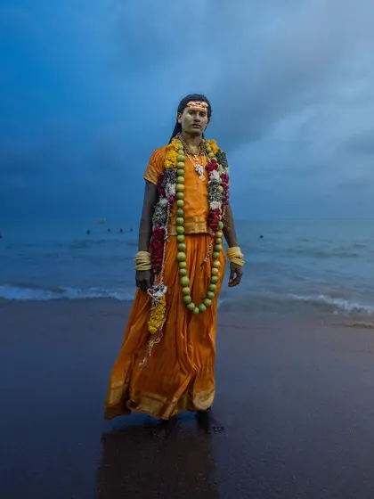 A Kulasai devotee stands at the edge of the sea at dusk, the vast ocean and moody sky providing a stunning backdrop for this cultural portrait.