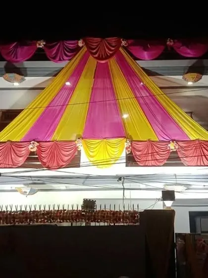 A tent-style canopy made of pink and yellow drapes covering the front of a house for a night event.