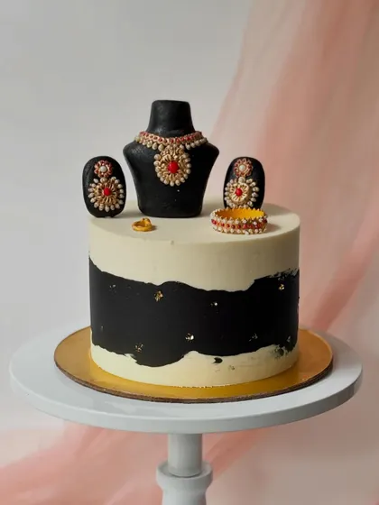 An elegant cake designed to look like a jewelry set. This is perfect for a jewelry lover, featuring a fondant necklace, earrings, and ring on a black and white buttercream cake.