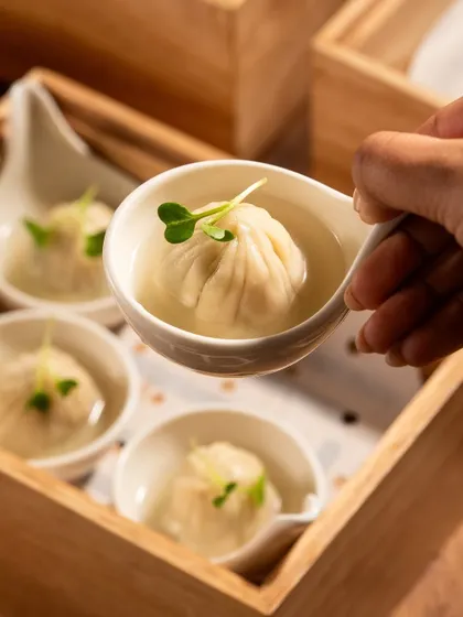 A close-up of a hand holding a soup dumpling. This brings a human element to the photo and shows the proper way to enjoy the dish.