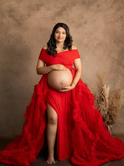 This portrait showcases a beautiful bare bump, celebrating the incredible transformation of a mother's body. The rich red gown frames the moment perfectly against a classic studio backdrop.