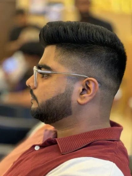 A sharp men's haircut focusing on the details. This style features a clean skin fade that blends seamlessly into a voluminous, textured top, paired with a perfectly lined-up beard.