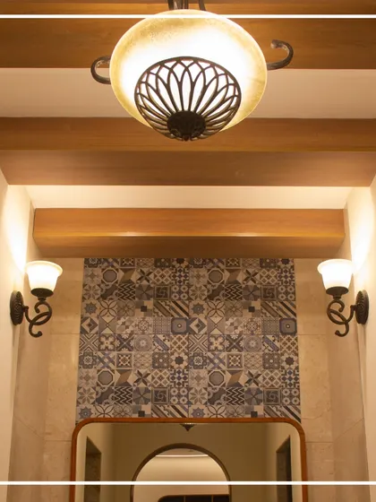 The lighting design in the gents' washroom combines a traditional chandelier with classic wall sconces. This layered approach provides both ambient and task lighting while reinforcing the modern heritage theme.