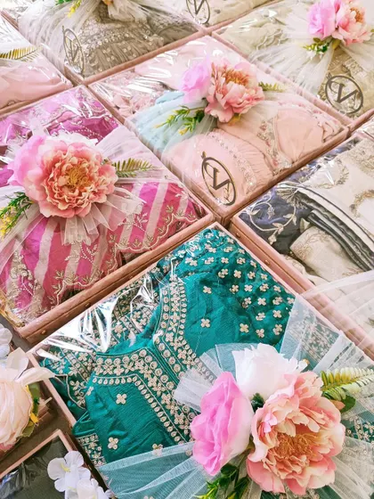 A vibrant collection of trousseau gifts, featuring a mix of bold and pastel colors. Each package is topped with a unique floral arrangement.