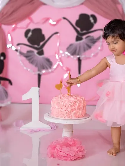 A little ballerina carefully places the 'one' candle on her cake, ready for her first birthday celebration.