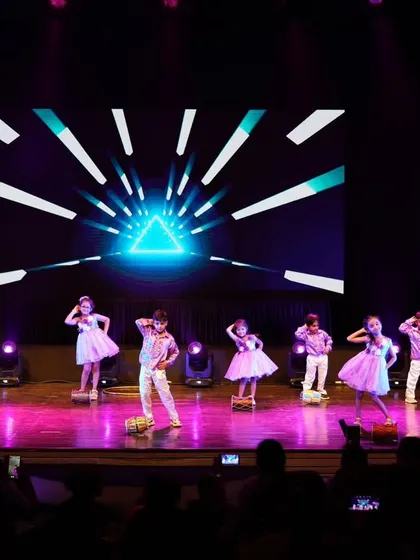 The entire stage filled with our little dancers during their prop-based Bollywood routine, set against a vibrant digital background.
